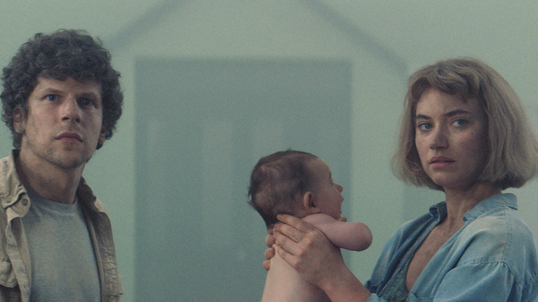 Gemma holds baby while standing in street with Tom in Vivarium