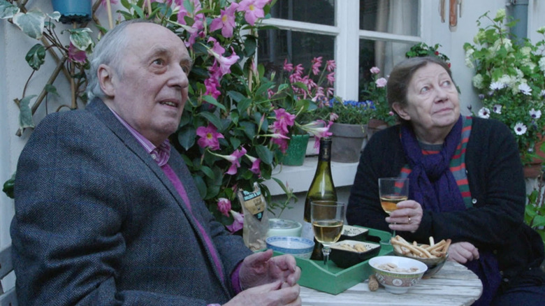 dario argento and françoise lebrun sitting at a garden table with wine in the movie vortex