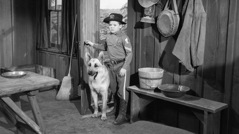 Rin Tin Tin IV and a boy dressed as a guard stand in the entrance of the cabin 
