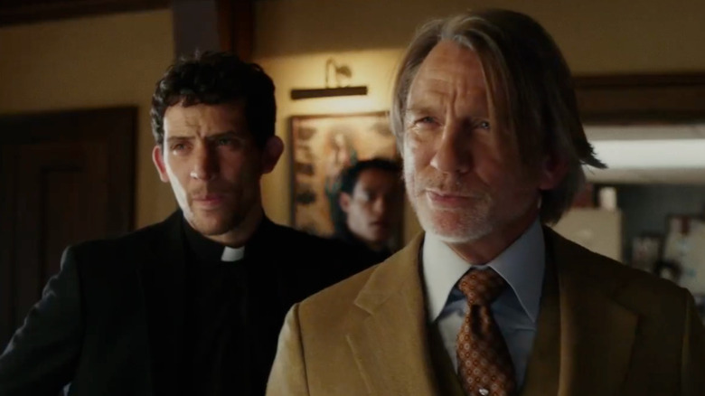 Benoit in a tan suit smirking with Jud and Cy behind him in Wake Up Dead Man