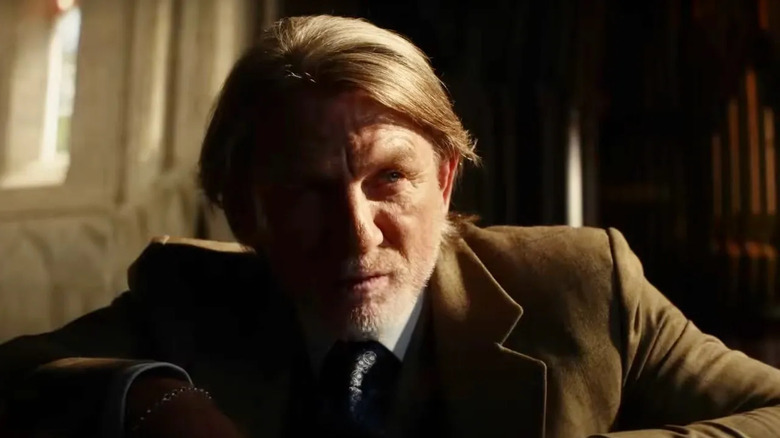 Blanc sitting in sunlight with longer hair and a tan jacket in Wake Up Dead Man