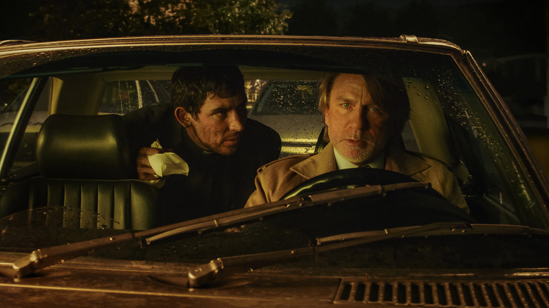 Josh O'Connor as Reverand Jud Duplenticy and Daniel Craig as Benoit Blanc sitting in a car in Wake Up Dead Man: A Knives Out Mystery