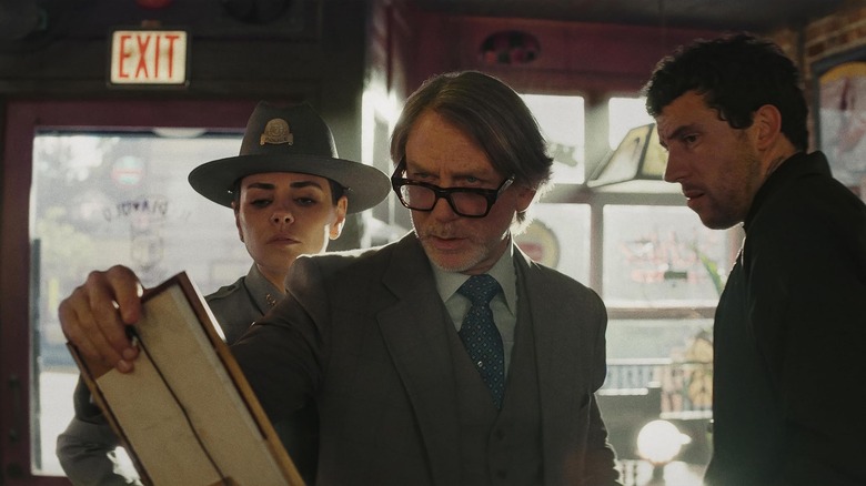 Benoit holidng up an item while Geraldine and Jefferson look on in Wake Up Dead Man: A Knives Out Mystery