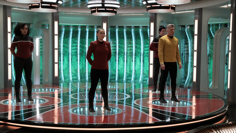 Christina Chong as La'an standing in the transporter room with Jack Quaid as Brad Boimler, Tawny Newsome as Beckett Mariner, and Anson Mount as Christopher Pike in Star Trek: Strange New Worlds