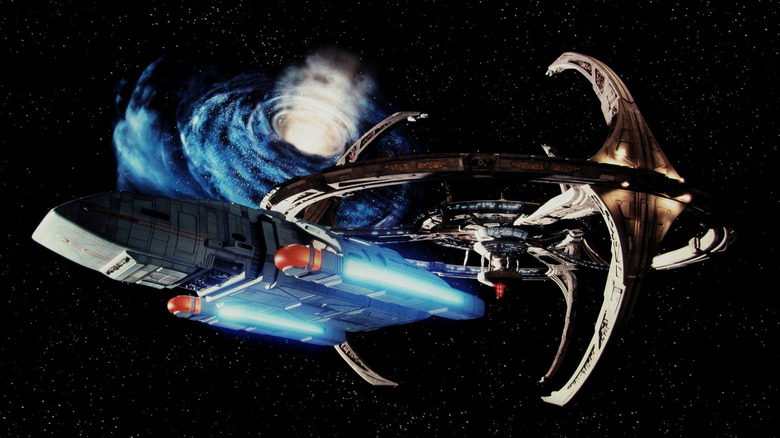 A spaceship passing in front of a space station with a wormhole emitting light in the background in Deep Space Nine