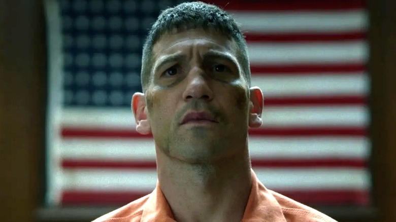 Jon Bernthal as Frank Castle/The Punisher wearing prison suit in front of American flag in Daredevil