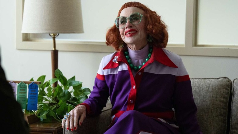 Gladys smiling with green glasses in Marcus' office on Weapons