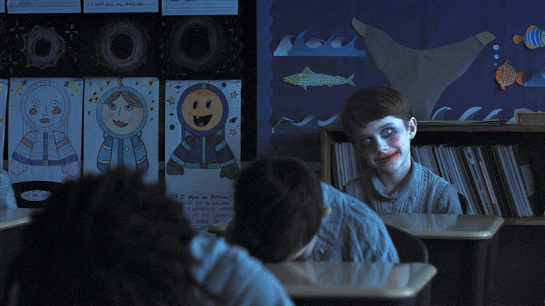 Alex smiling creepily with clown makeup on in the classroom in Weapons