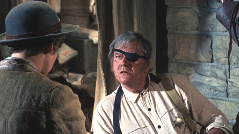 John Wayne's Reuben "Rooster" J. Cogburn looks shocked as he sits up while talking to Kim Darby's Mattie Ross in True Grit