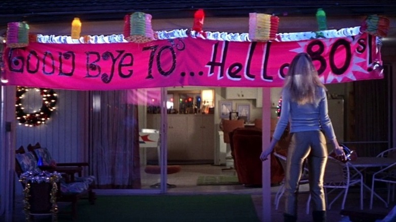 Heather Graham in Boogie Nights, standing next to a banner that says "Goodbye 70's... Hello 80's"