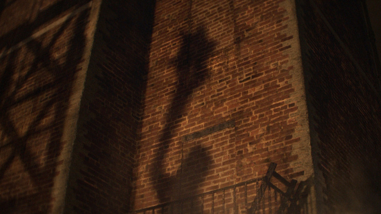 The shadow of Clayface's club hand on a brick wall in Clayface