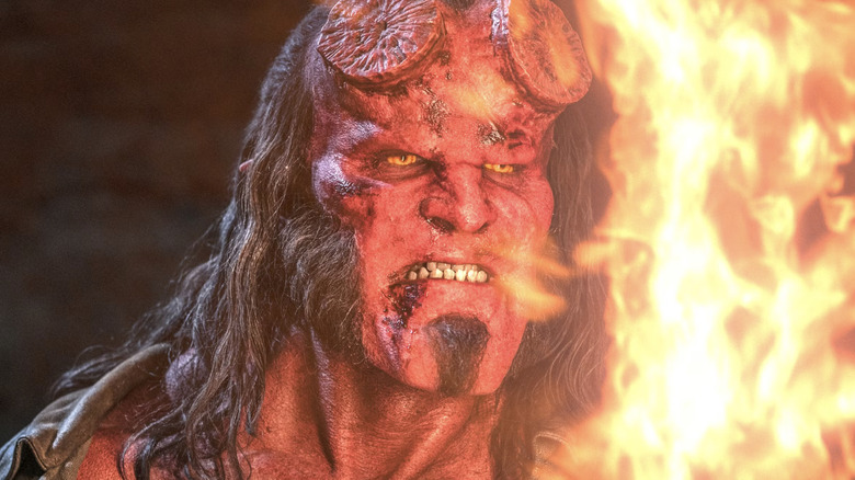 David Harbour as Hellboy, looking at his flaming sword Excalibur, in Hellboy (2019)