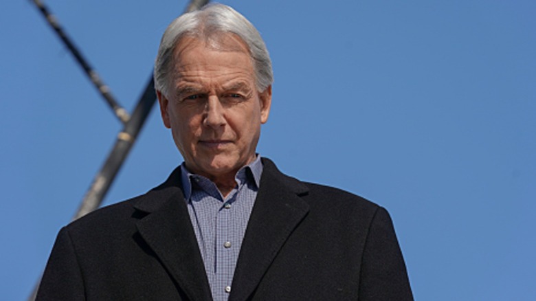Mark Harmon's Jethro Gibbs looks down while standing against a blue sky in NCIS