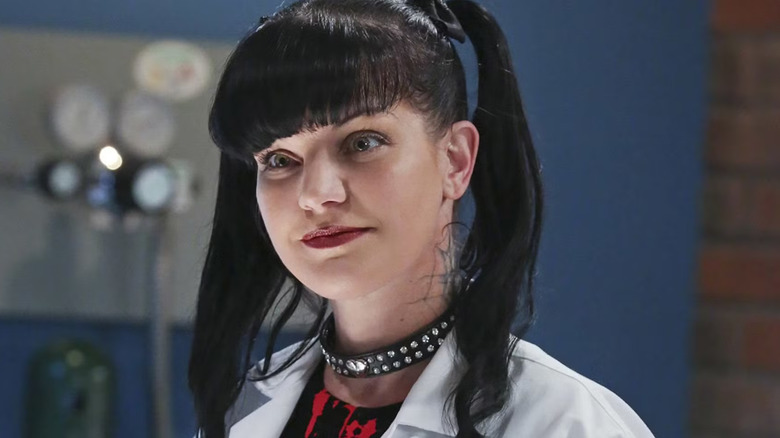 Abby, with her bangs and leather choker and lab coat, looking interested. A scene from NCIS.