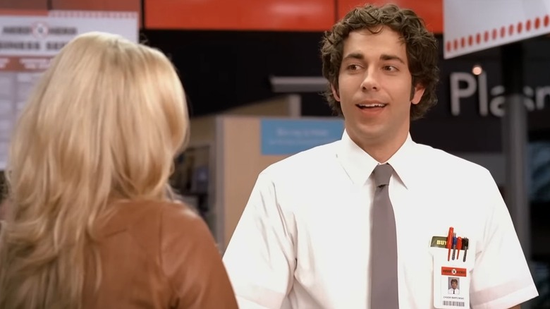 Zachary Levi as Chuck on Chuck, in his Buy More uniform, smiling at Sarah