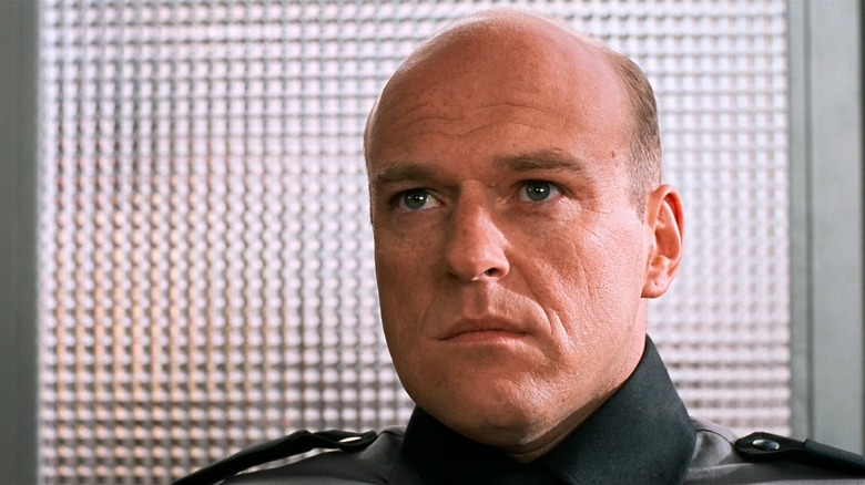 Dean Norris as a Commanding Officer in Starship Troopers, sitting in front of a lit window