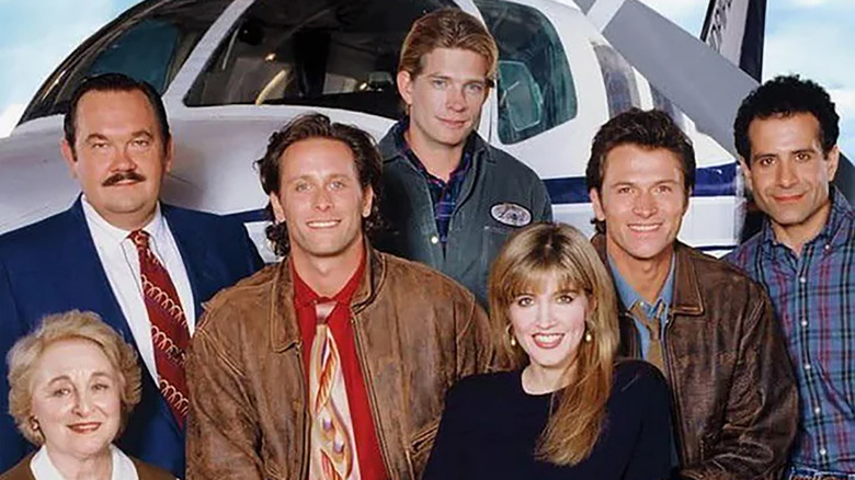 Rebecca Schull as Fay, David Schramm as Roy, Steven Weber as Brian, Thomas Haden Church as Lowell, Crystal Bernard as Helen, Tim Daly as Joe, and Tony Shalhoub as Antonio, posing for a group shot in front of the primary plane in Wings.