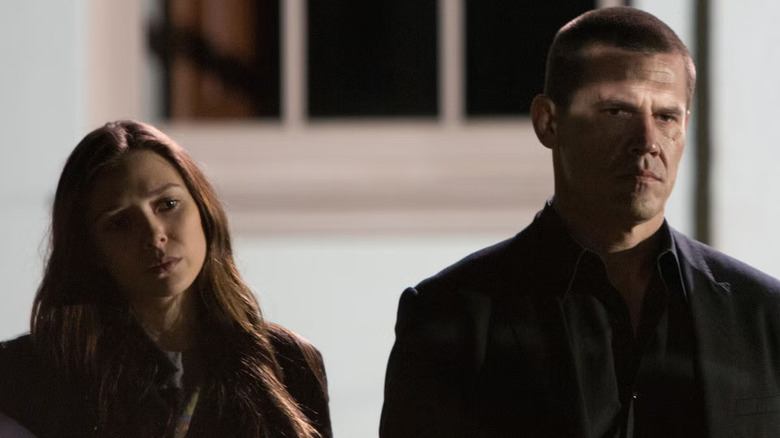 Josh Brolin (Joe) and Elizabeth Olsen (Marie) wear dark office clothes and serious expressions, their faces shadowed against a white background with a window behind them in Oldboy