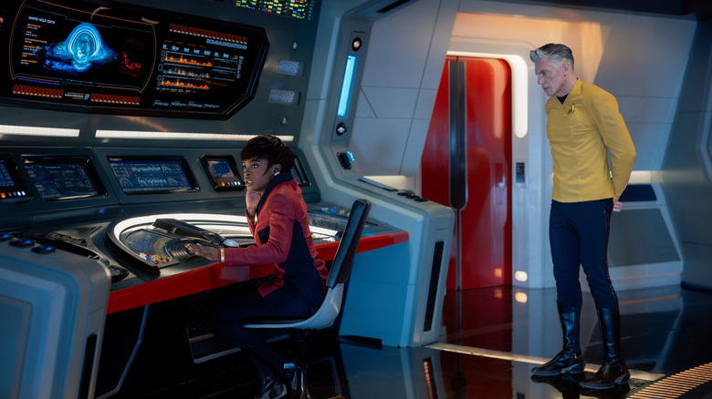 Celia Rose Gooding as Nyota Uhura sitting at her console while Anson Mount as Christopher Pike stands behind her in Star Trek: Strange New Worlds