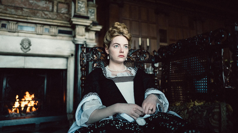 Abigail sitting in a fine gown on a carved chair looking bored and annoyed in The Favourite