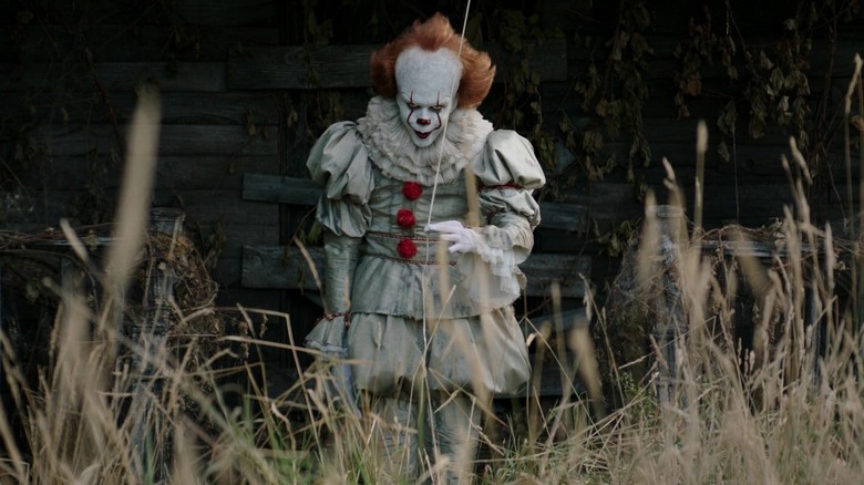 Pennywise the clown standing in the weeds