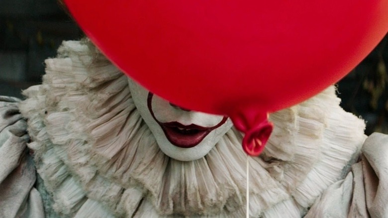 Bill Skarsgard as Pennywise holding a red balloon in front of his face in IT (2017)