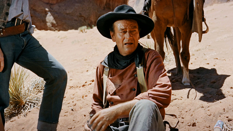John Wayne as Ethan Edwards sits holding a water canteen in The Searchers