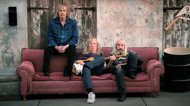 Christopher Guest, Michael McKean, and Harry Shearer as Nigel, David, and Derek sitting on a couch for a photoshoot in Spinal Tap 2