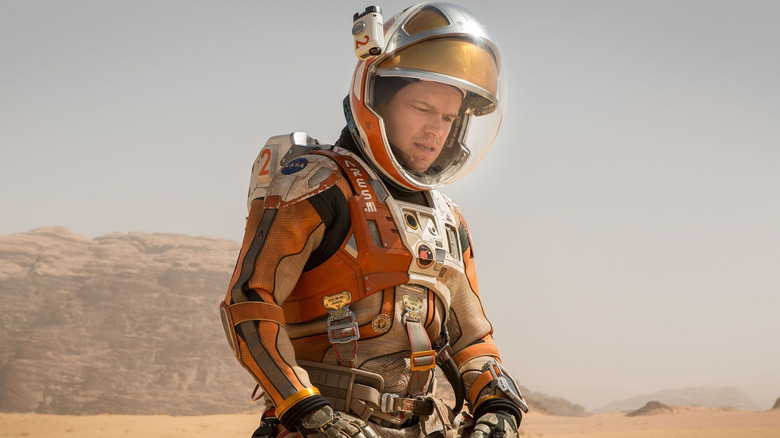 Matt Damon as Mark Watney kneeling in the sand on Mars in The Martian