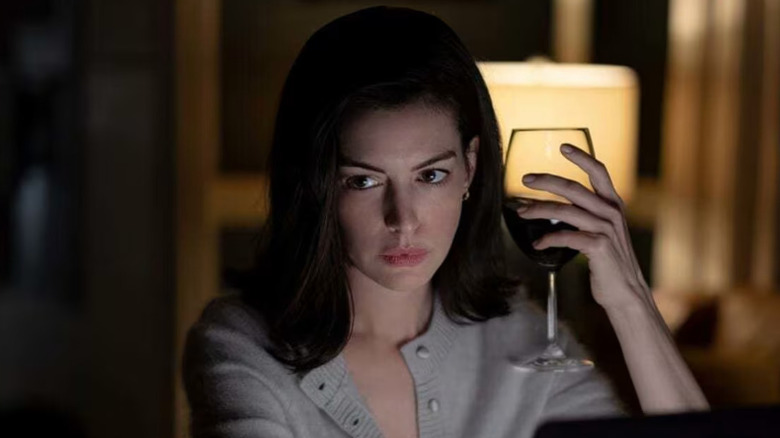 Anne Hathaway as Verity Crawford sitting at her desk with a glass of wine in Verity