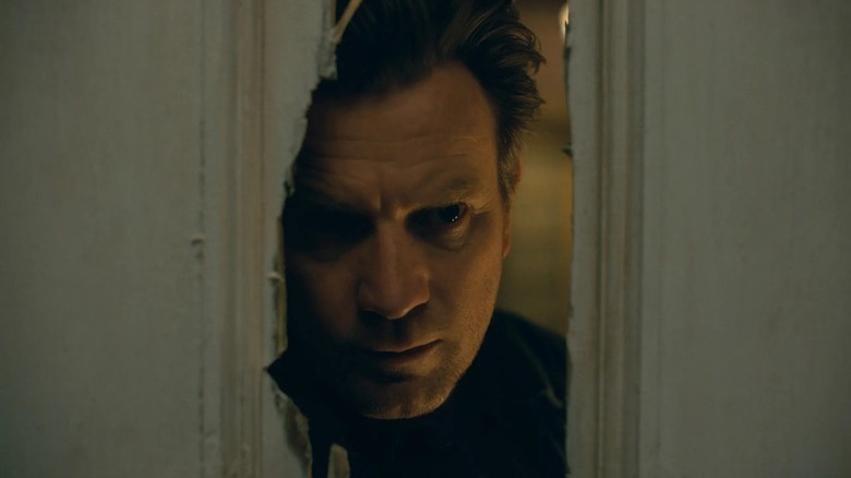 Ewan McGregor's Dan Torrance looking through a broken door in Doctor Sleep