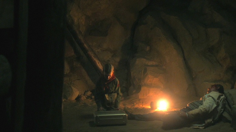 Young Henry Creel (wearing a scout uniform) opens a briefcase in a mine on Stranger Things