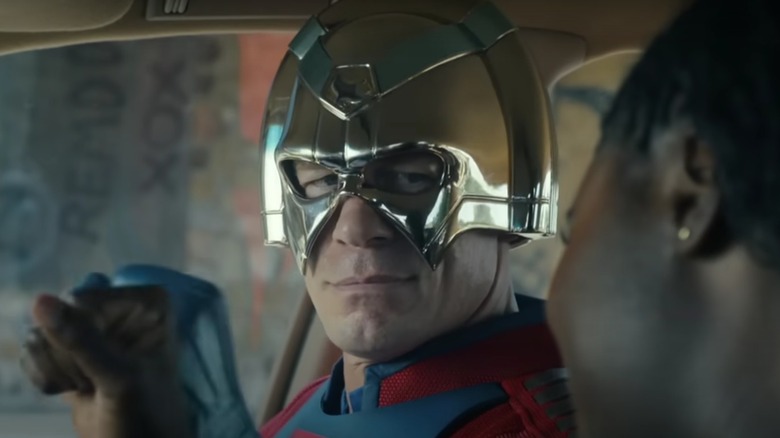 John Cena as Peacemaker wearing his vigilante costume and smiling sadly on Peacemaker