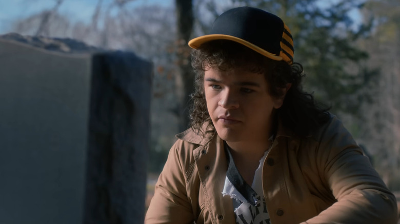 Dustin kneeling before Eddie Munson's gravestone in Stranger Things season 5