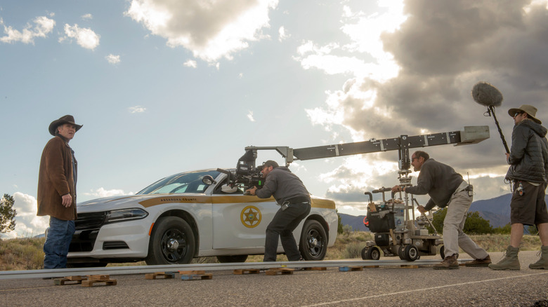 A film crew shoots Robert Taylor as Sheriff Walt Longmire while he stands next to a police car on the set of Longmire