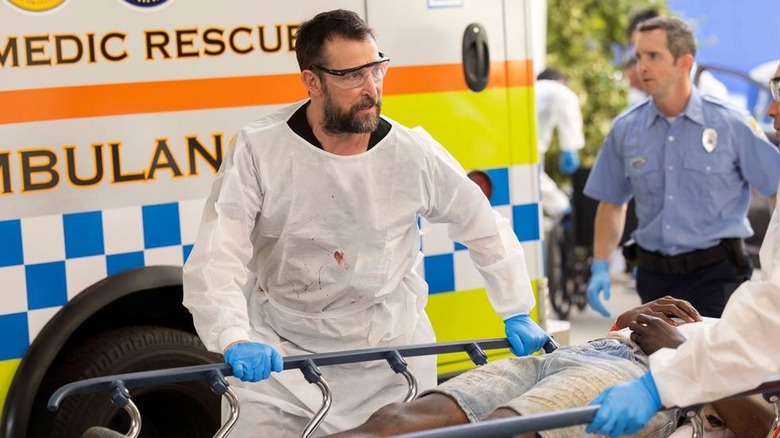 Dr. Noah Will, in full protection equipment, draws a stretcher away from an ambulance in a house