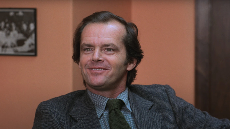 Jack Nicholson's Jack Torrance smiles as he sits in an office in The Shining