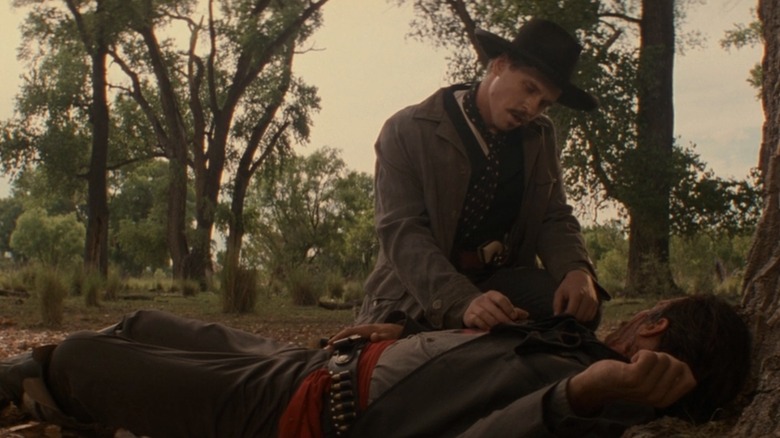 Val Kilmer as Doc Holliday crouching next to someone on the ground in Tombstone