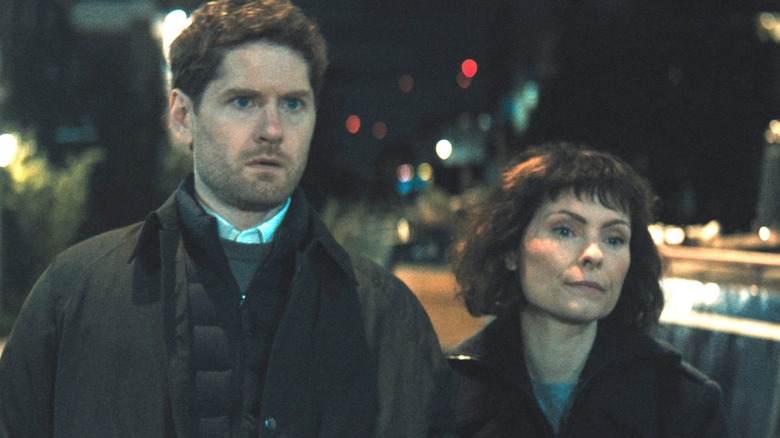 Kyle Soller as Jim standing arm-in-arm with MyAnna Buring as Jane while walking down an empty street at night in Slow Horses