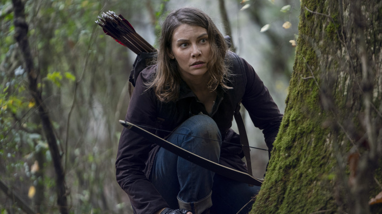 Lauren Cohan as Maggie Greene kneeling by a tree with her bow and arrow in The Walking Dead