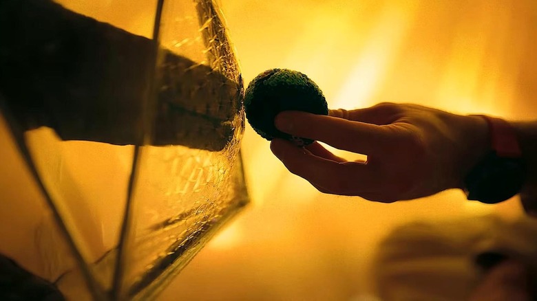 Close-up of Ryland Grace holding a bean bag juggling ball of Earth out to Rocky in Project Hail Mary