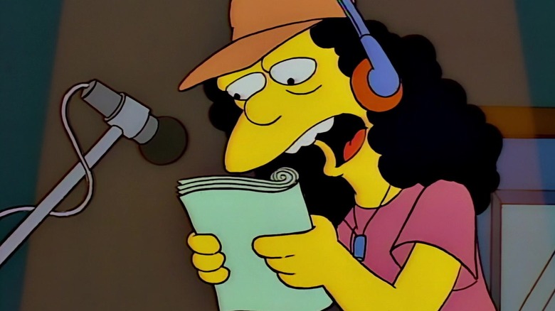 Otto, reading from a page, wearing headphones, standing at a mic. A spotlight shines on him. A scene from The Simpsons.