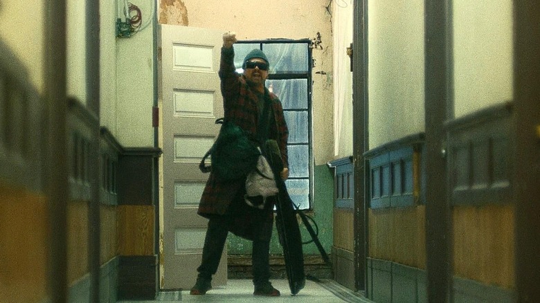 Leonardo DiCaprio as Bob Ferguson wearing sunglasses and a bathrobe raising his fist in solidarity in One Battle After Another