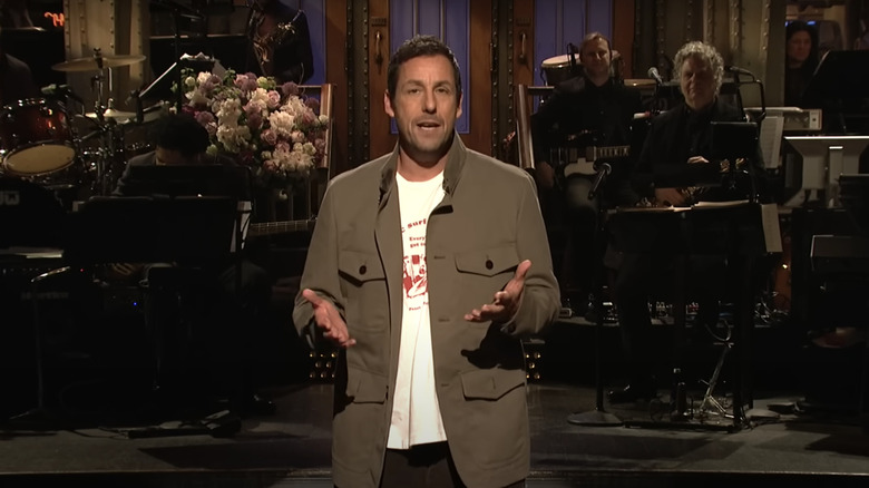 Adam Sandler standing onstage, hosting Saturday Night Live in 2019