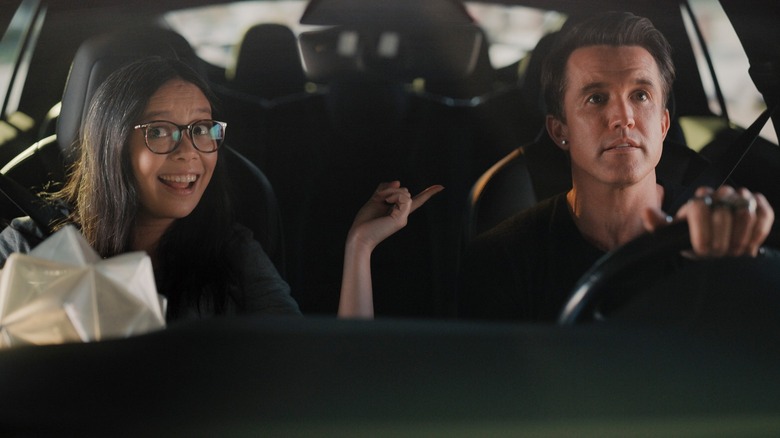 Charlotte Nicdao as Poppy smiles while sitting beside Rob McElhenney as Ian, who is driving a car, in Mythic Quest