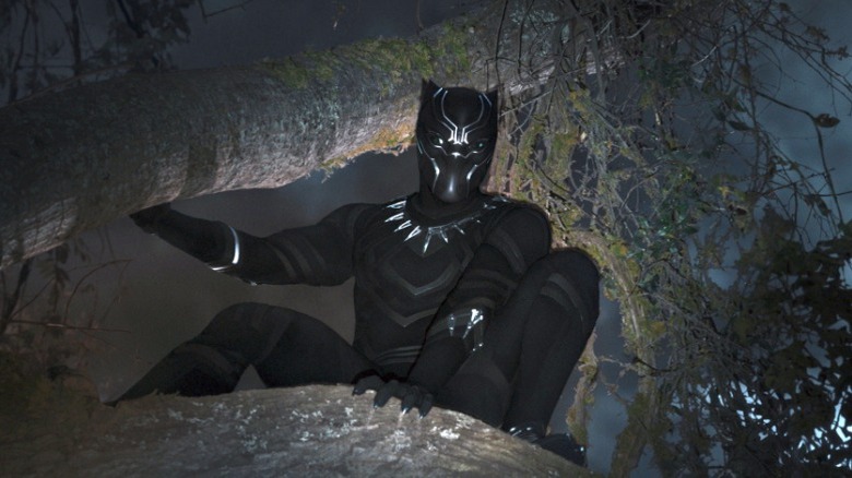 Black Panther poses in a tree while someone shines a light on him in Black Panther (2018)