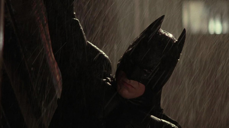 Batman hanging from a ledge in the rain in Batman Begins
