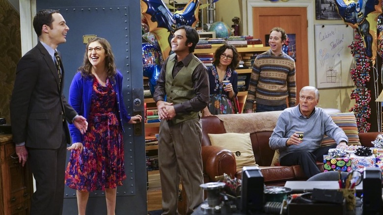 Sheldon enters a room full of merry-makers, everyone is smiling. Adam West is on the couch, looking panicked.