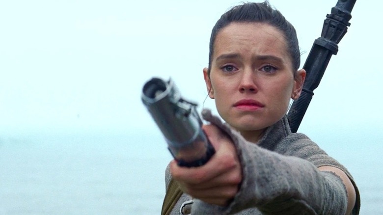 Daisy Ridley as Rey holds out a lightsaber in Star Wars: Episode VII - The Force Awakens