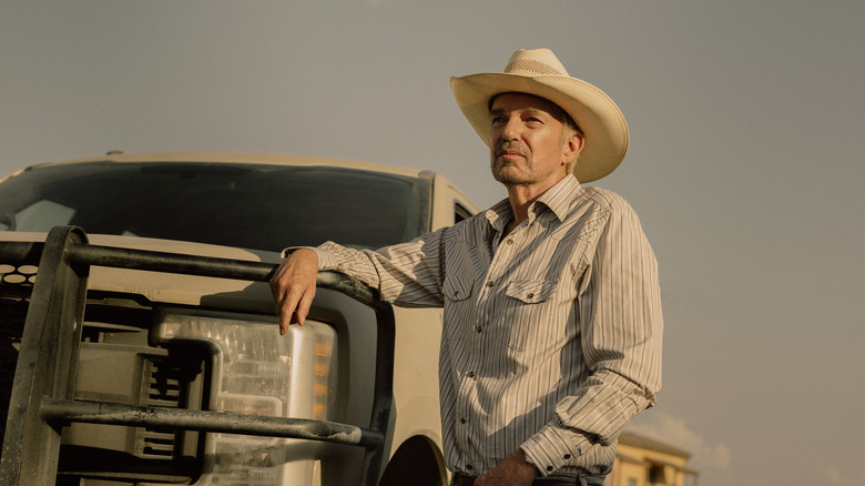 Billy Bob Thornton's Tommy Norris rests his arm on a truck as he stands against a clear sky in Landman.jpg